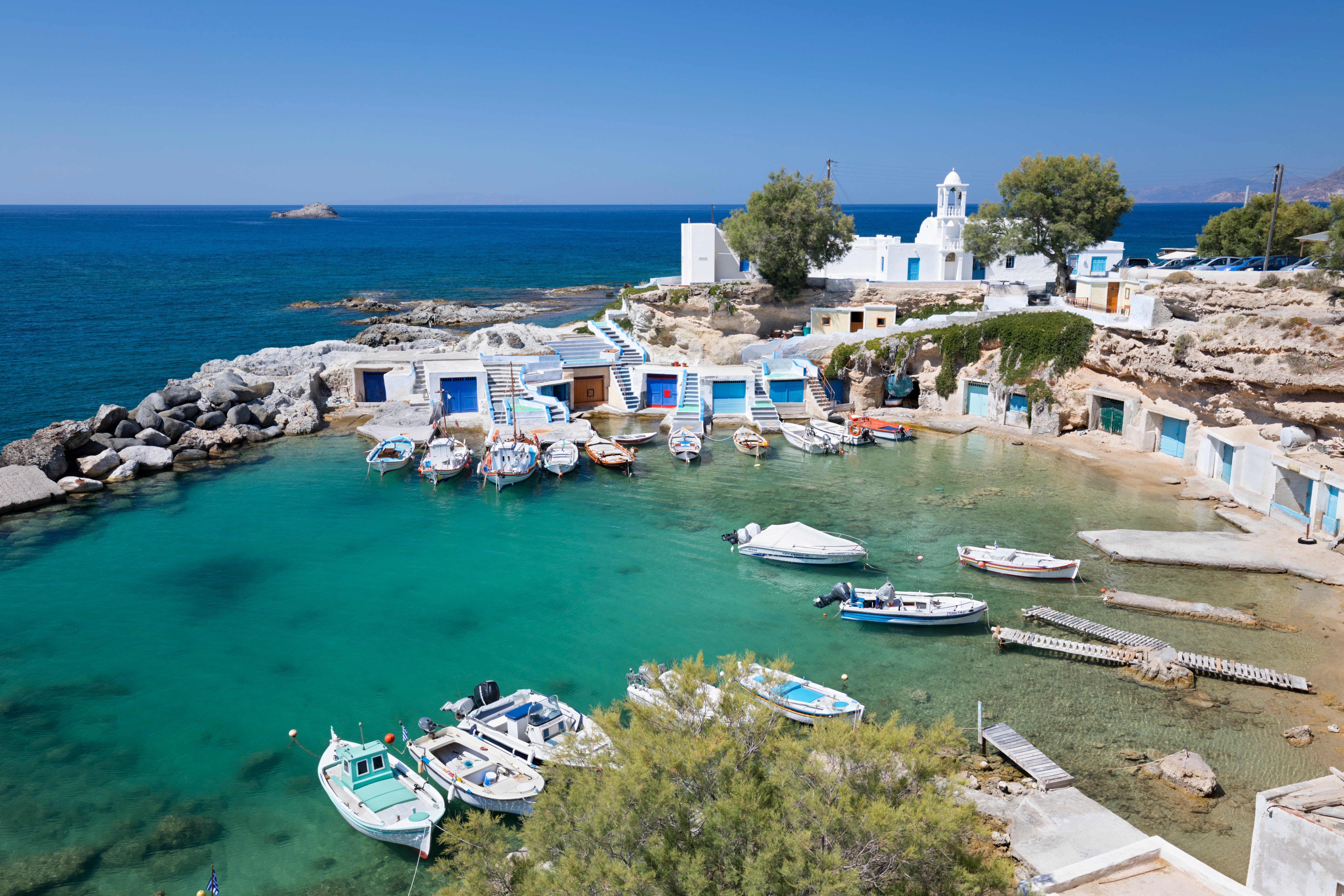 Fishing boats in a small harbour with whitewashed houses in Milos, Greece